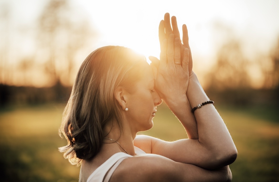 Hält die Hände über dem Kopf zusammen, die Abendsonne scheint durch die Finger